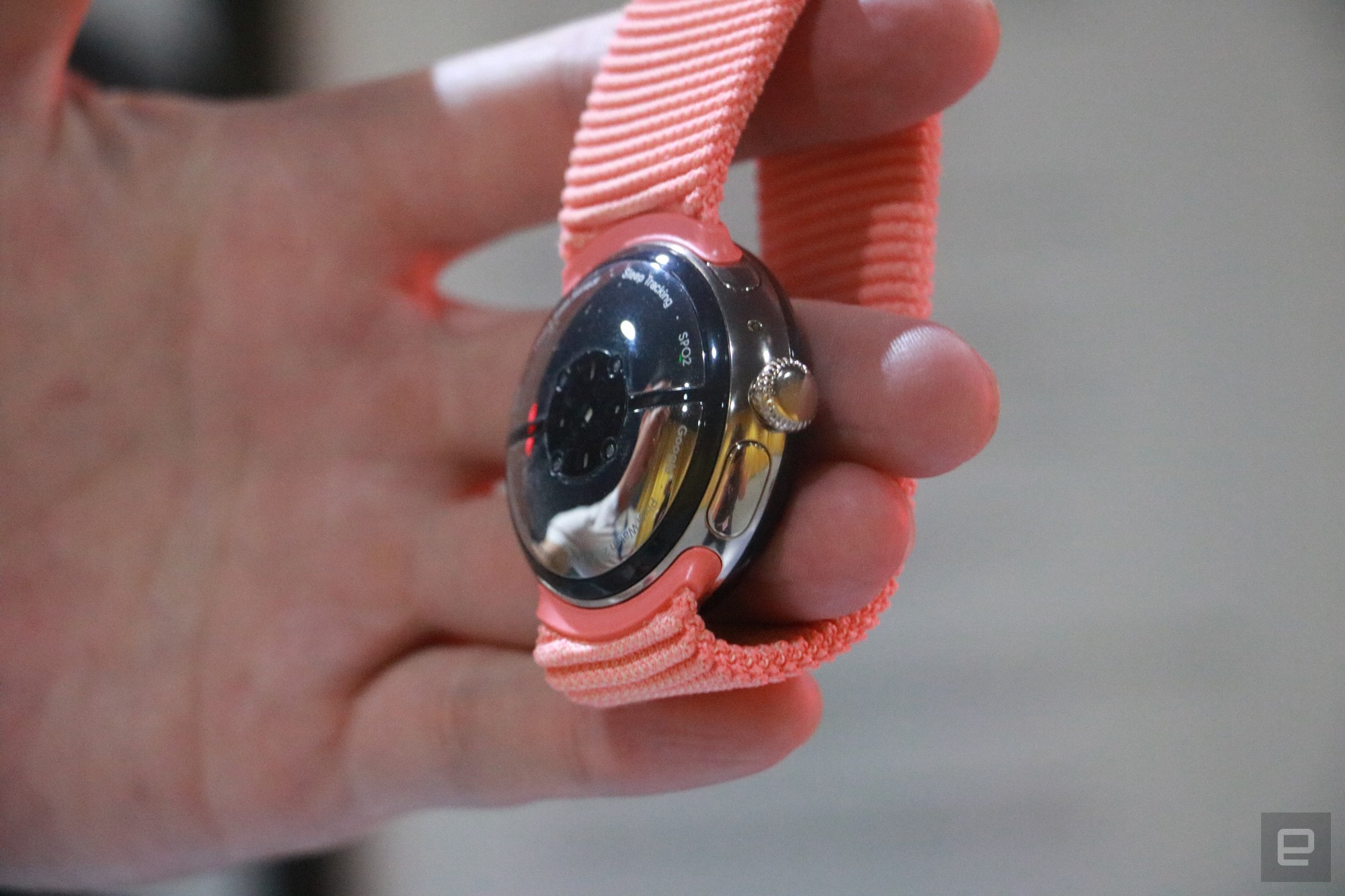 A side view of the underside of the Pixel Watch 2, showing its charging setup and new sensors, as well as the crown and button on the bezel.
